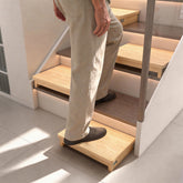 Person using a wooden half-step stool on an indoor staircase, with additional half steps positioned on the stairs.