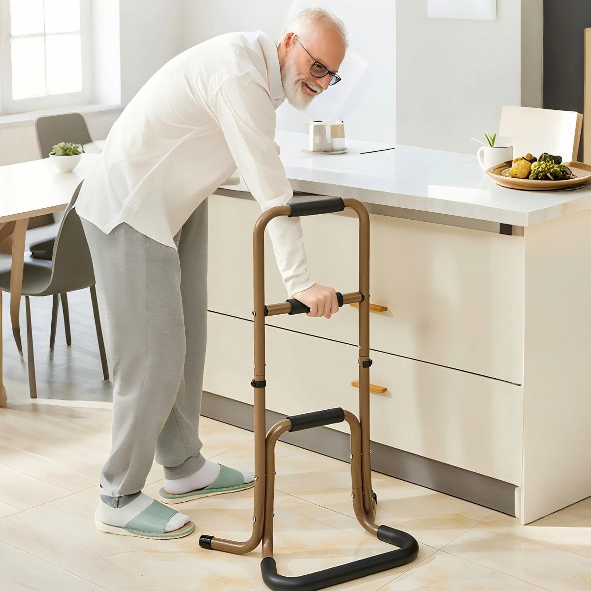 Older man using a brown portable stand assist beside a kitchen counter, gripping the padded middle handle for standing support.