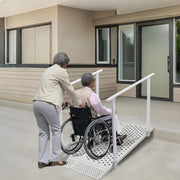 Caregiver pushing a wheelchair user up a white wheelchair ramp with handrails toward a building entrance.