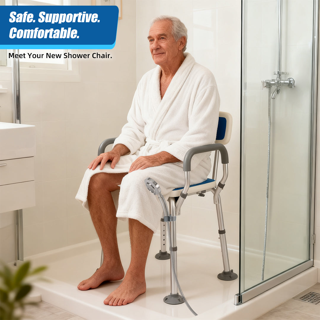 Older man in a white bathrobe seated on a shower chair with padded armrests and backrest, with a handheld shower head beside the seat.