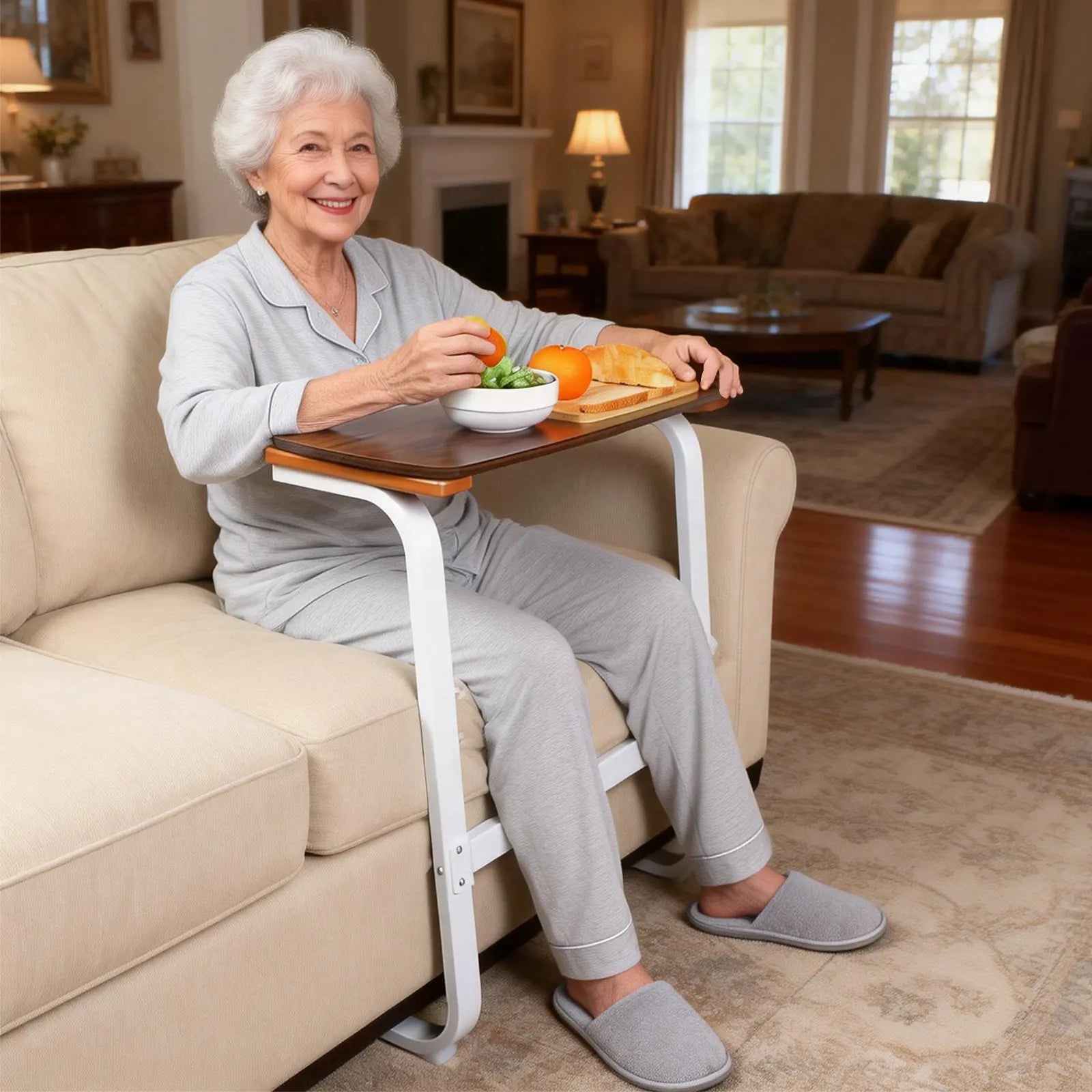 Older woman seated on a sofa using the wooden tray table for a meal, with the white sit-to-stand assist frame positioned in front of her.