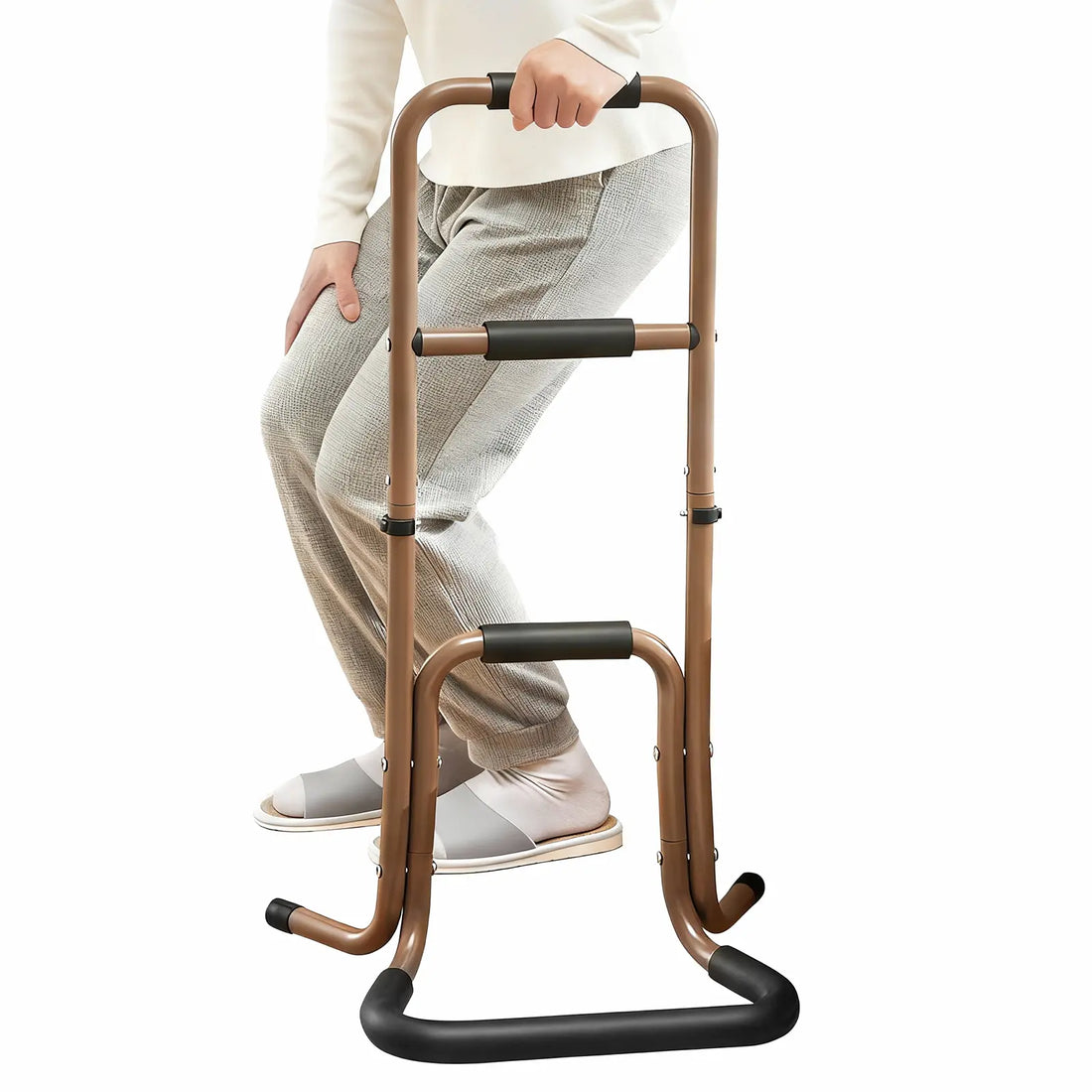 Person rising from a seated position while holding a brown portable stand assist with three foam-padded hand grips and a wide floor base.