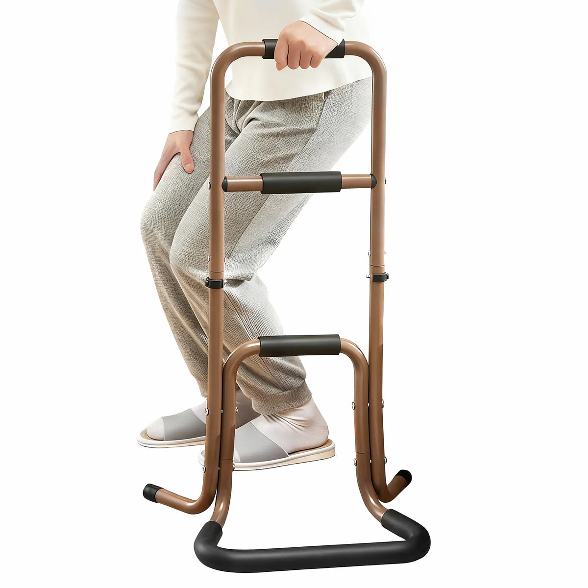 Person rising from a seated position while holding a brown portable stand assist with three foam-padded hand grips and a wide floor base.