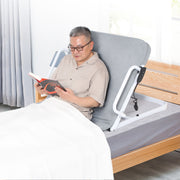 Man reading in bed while supported by a raised gray electric bed backrest, with side support rails and a wired controller visible.