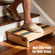 Wooden half-step stool positioned on an indoor staircase, with black non-slip strips across the platform and a person stepping onto it.