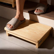 Close-up of a person using a wooden half-step stool between two stair levels, with one foot on the platform and the other on the upper stair.