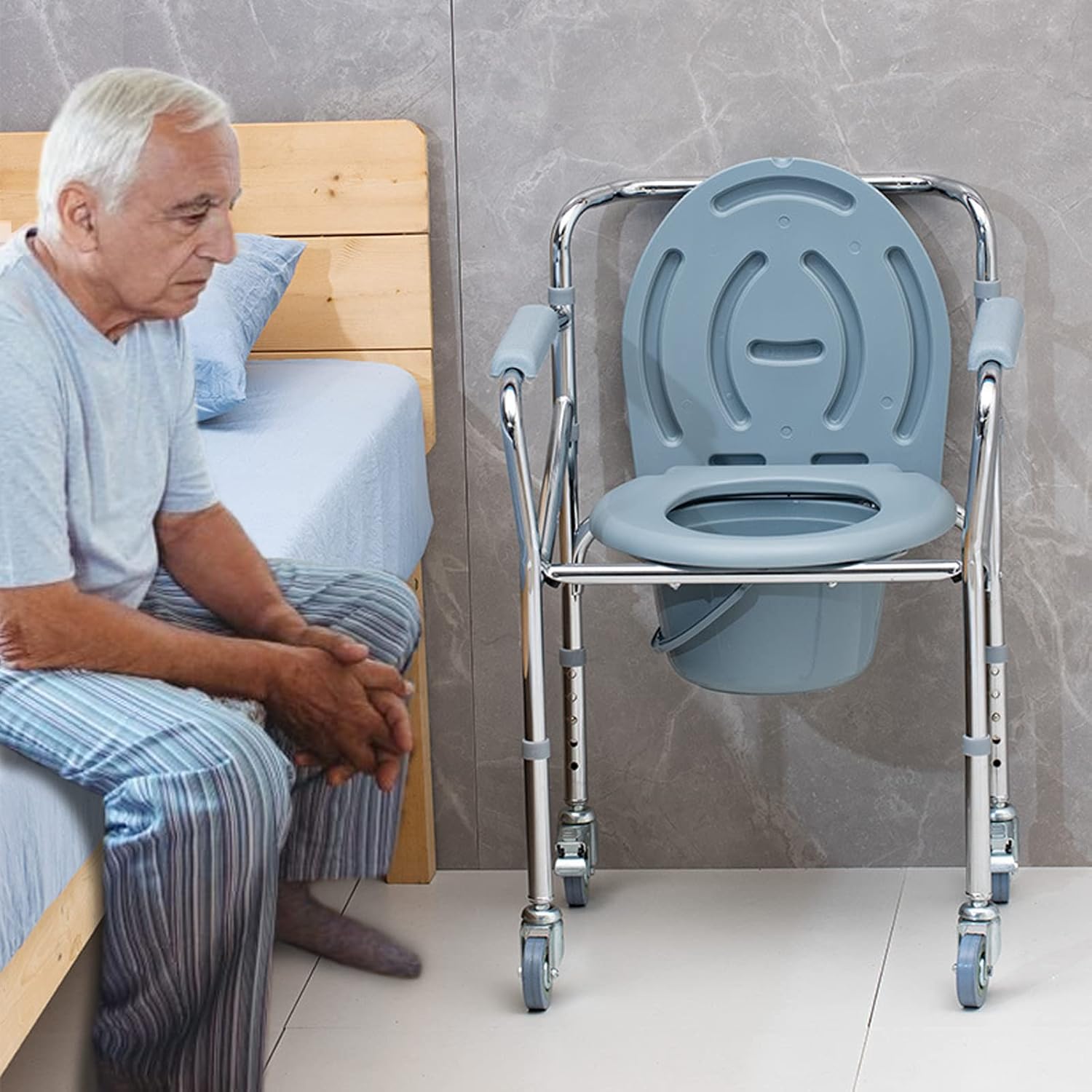 Older man seated on the edge of a bed beside a portable bedside commode chair with wheels, padded armrests, and a removable pail.