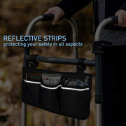 Black walker storage bag attached to a folding walker in a dark outdoor setting, with reflective strips along the three front pockets illuminated.