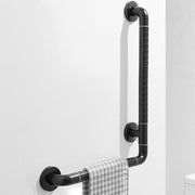 Black 16 x 24 inch L-shaped bathroom grab bar mounted on a wall, with textured grip sections, circular mounting plates, and a towel hanging from the horizontal rail.