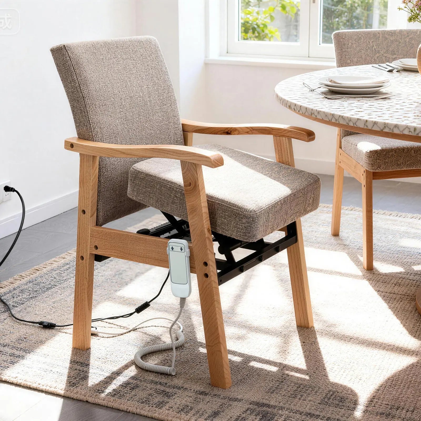 Wooden power lift assist chair with gray fabric upholstery, padded armrests, an under-seat lifting mechanism, and a wired controller, shown beside a dining table.