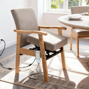 Wooden power lift assist chair with gray fabric upholstery, padded armrests, an under-seat lifting mechanism, and a wired controller, shown beside a dining table.